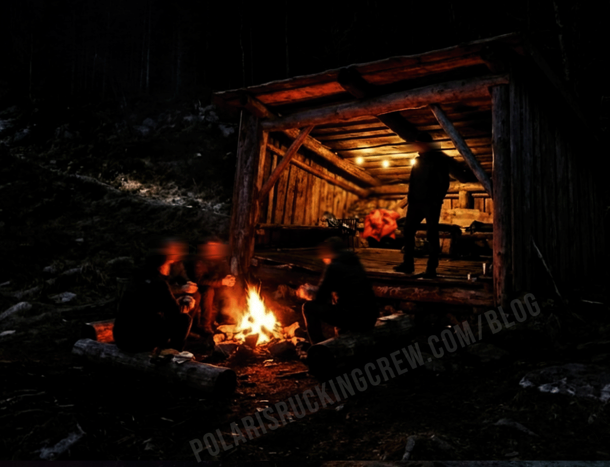 A group gathered around a fire beside a wooden shelter at night